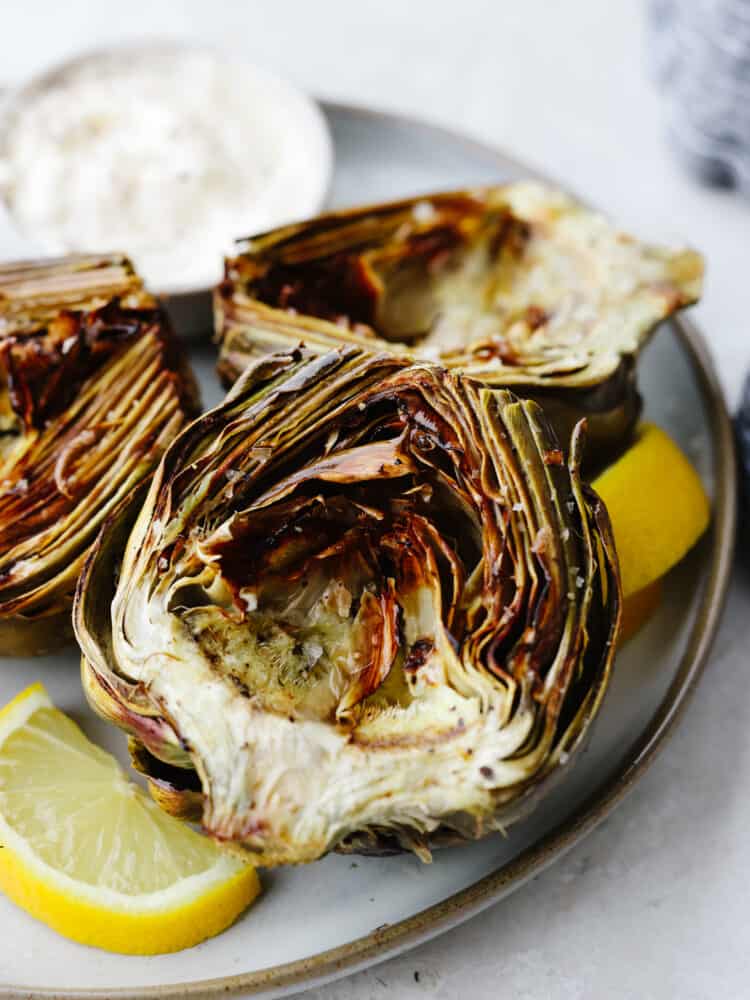 Cooked artichokes on a plate with lemon slices. 
