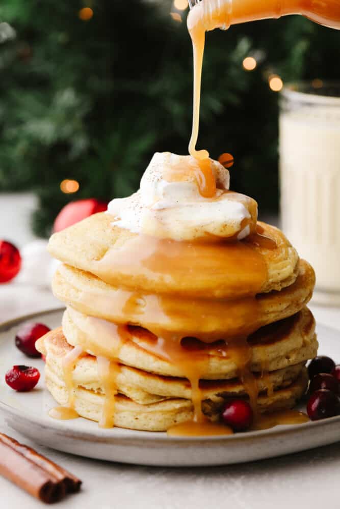 Caramel sauce being drizzled onto a stack of eggnog pancakes. 