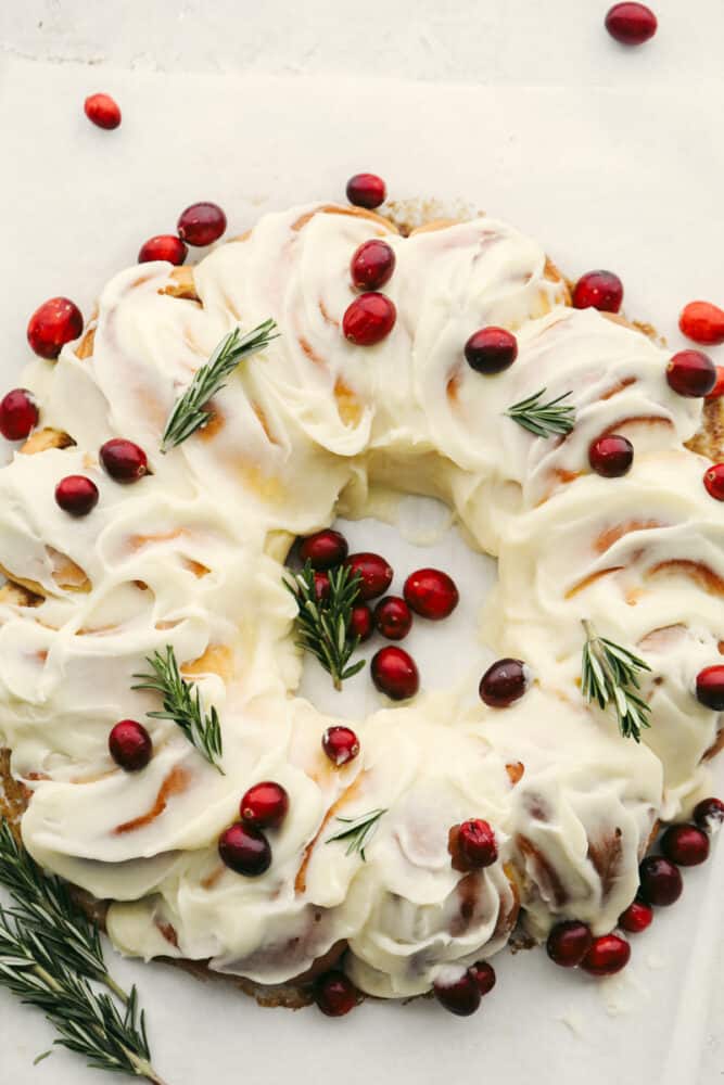 A cinnamon roll wreath with cranberries and green garnish. 