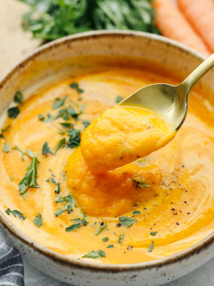 A spoon scooping carrot soup out of a bowl. 