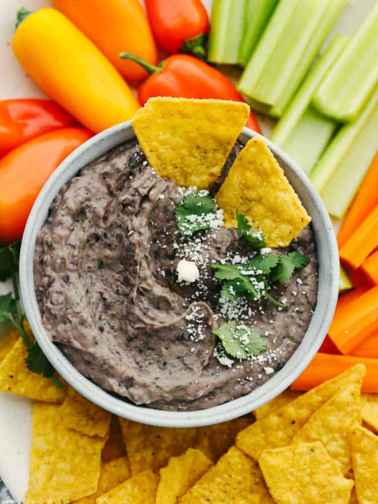 Closeup of black bean dip surrounded by an assortment of chips and vegetables.