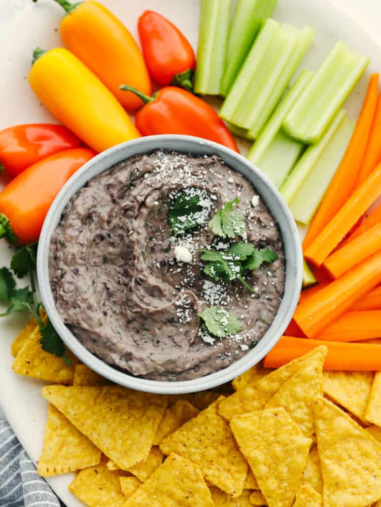 Black bean dip in a white bowl, surrounded by chips and vegetables.