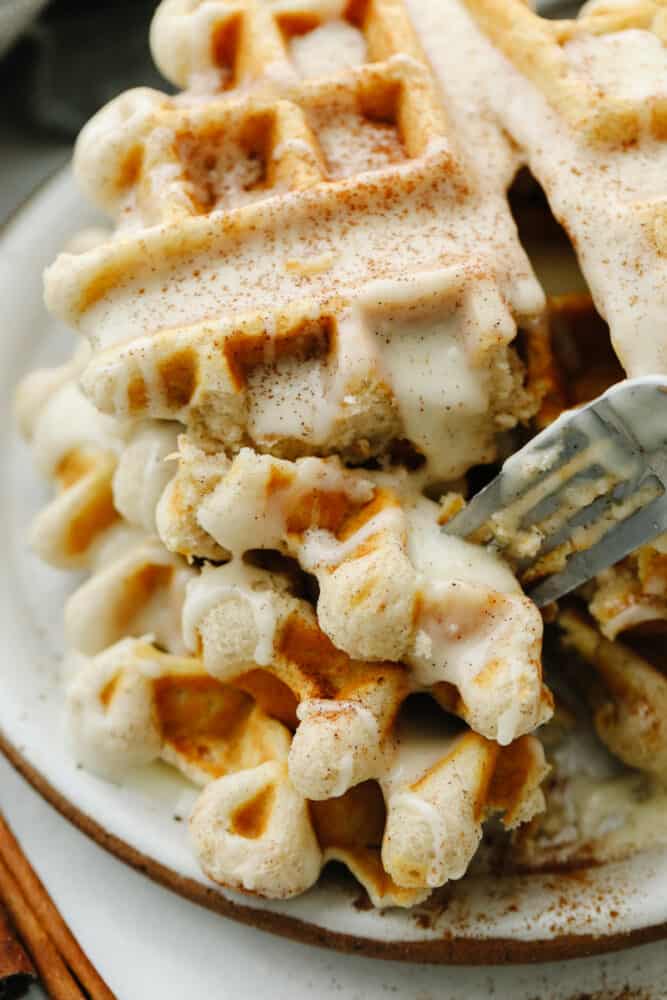 A cinnamon roll waffle being cut into with a fork. 