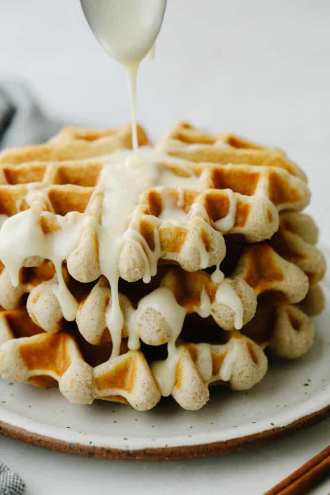 A cinnamon roll waffle with cream cheese glaze being drizzled on it. 