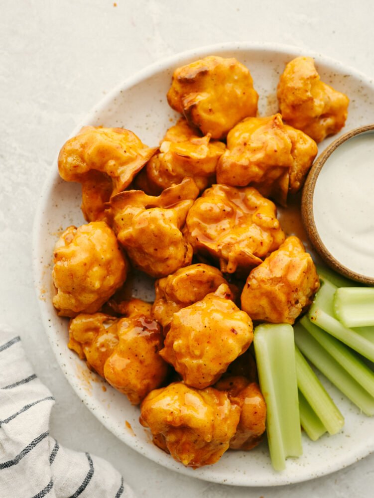 Air fryer honey buffalo cauliflower wings served on a white stoneware plate alongside ranch and celery.