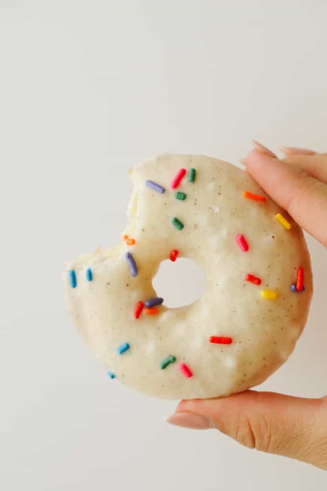 A cake donut being held that is half eaten.