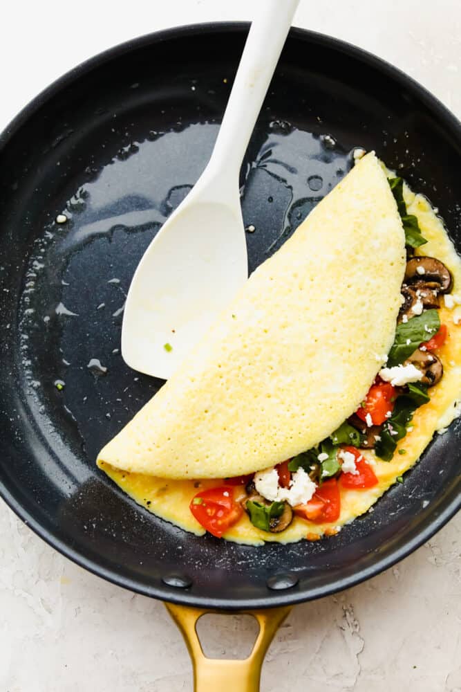An omelet in a pan, filled with ingredients being folded in half.