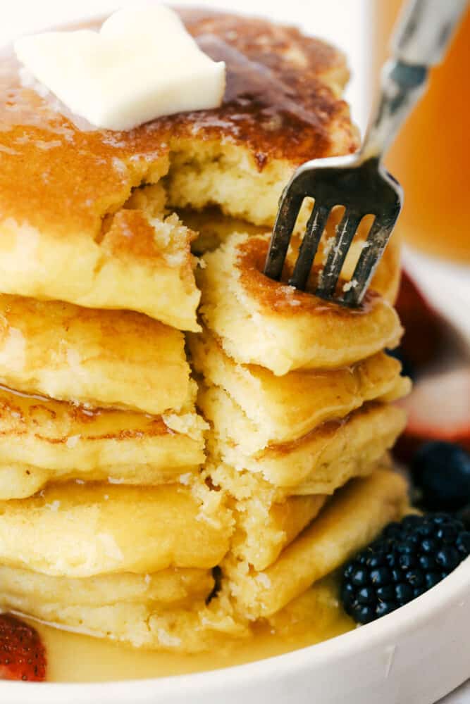Using a fork to take a bite out of the stack of cornmeal pancakes. 