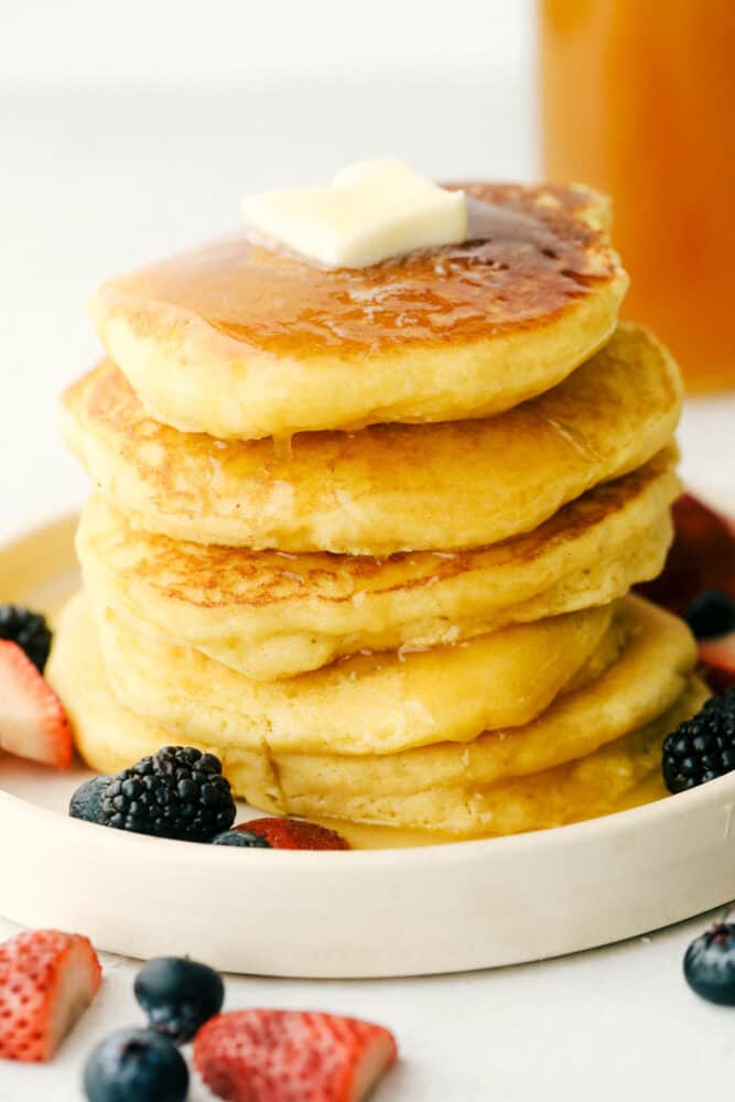 A stack of cornmeal pancakes dripping in honey butter syrup. 