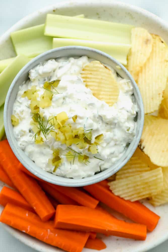 Dill pickle dip on serving dish with chips and veggies.