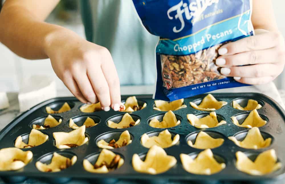 Crescent rolls being placed in a muffin tin sprinkled with pecans. 