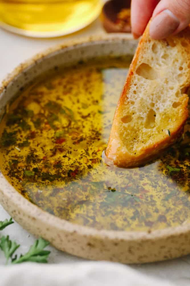A slice of bread being dipped into olive oil dip. 