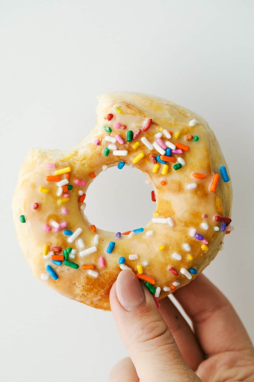 Holding a donut with sprinkles and bite out of it.