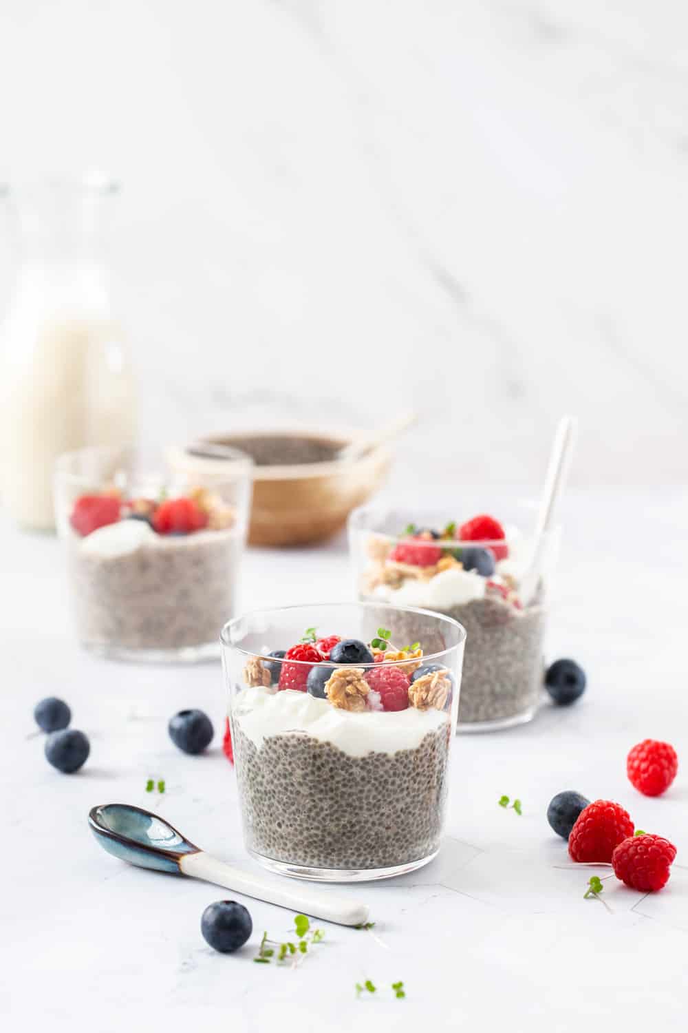 3 chia puddings in glasses topped with berries and granola.