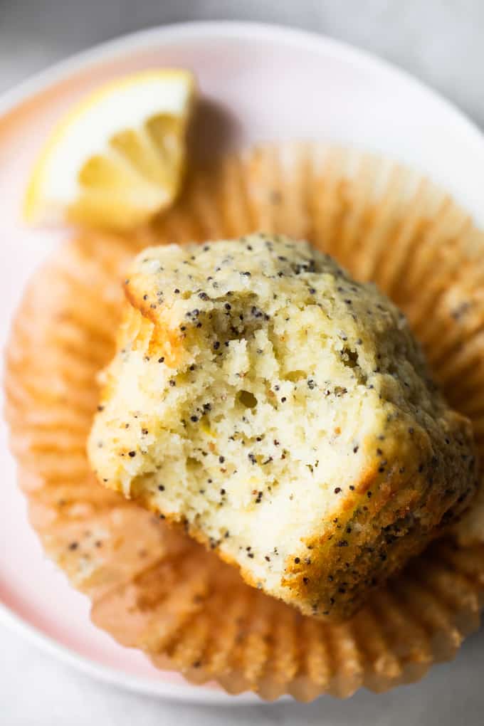 Poppyseed muffin with a bite out of it and on the plate with a lemon slice as a garnish. 