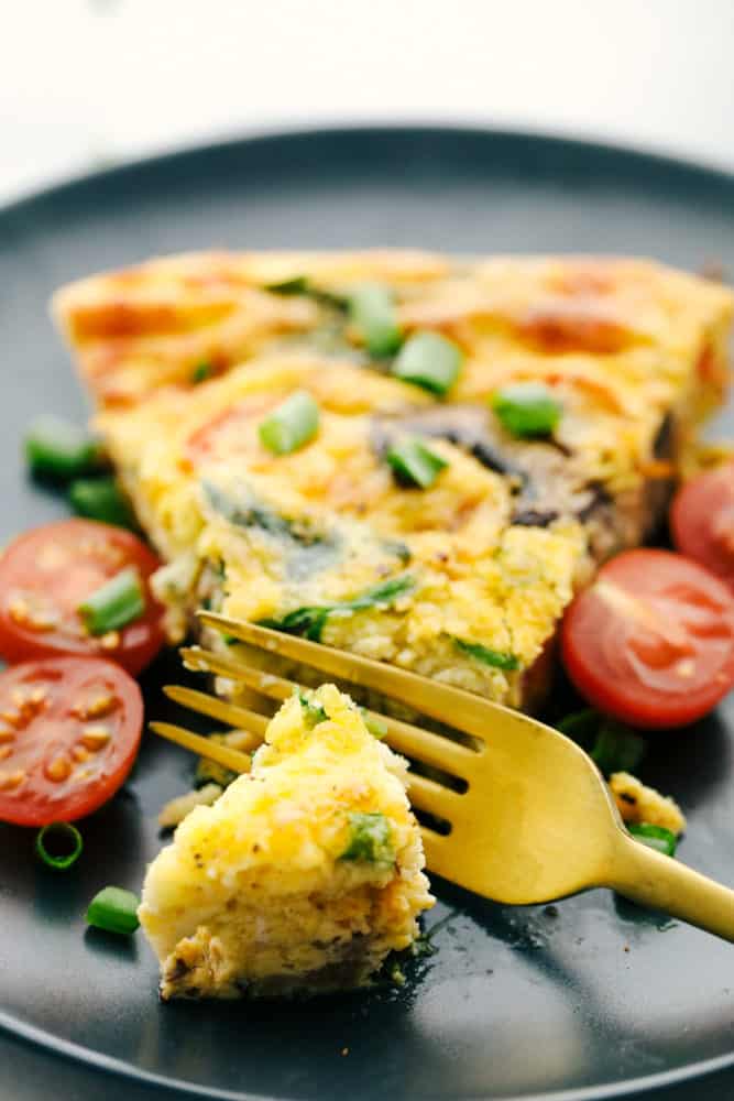 Breakfast frittata on a plate with a piece cut off with cherry tomatoes sliced on the side. 