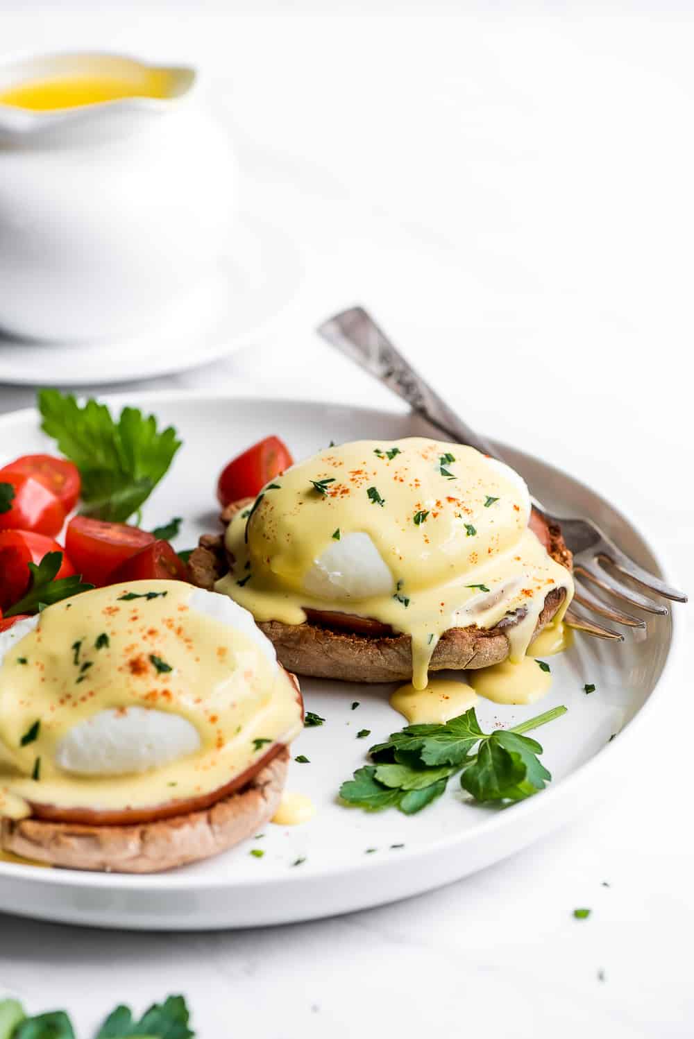 Two Eggs Benedict on a plate with hollandaise dripping off of them.