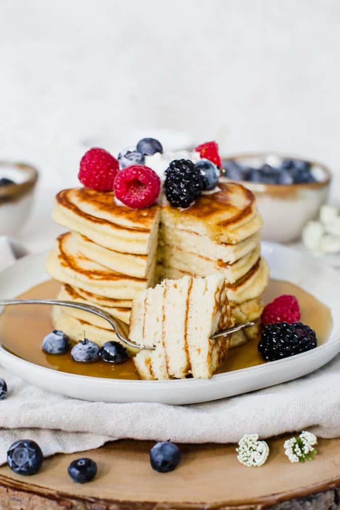 Keto pancakes stacked together with fresh fruit and whipped topping on top. 