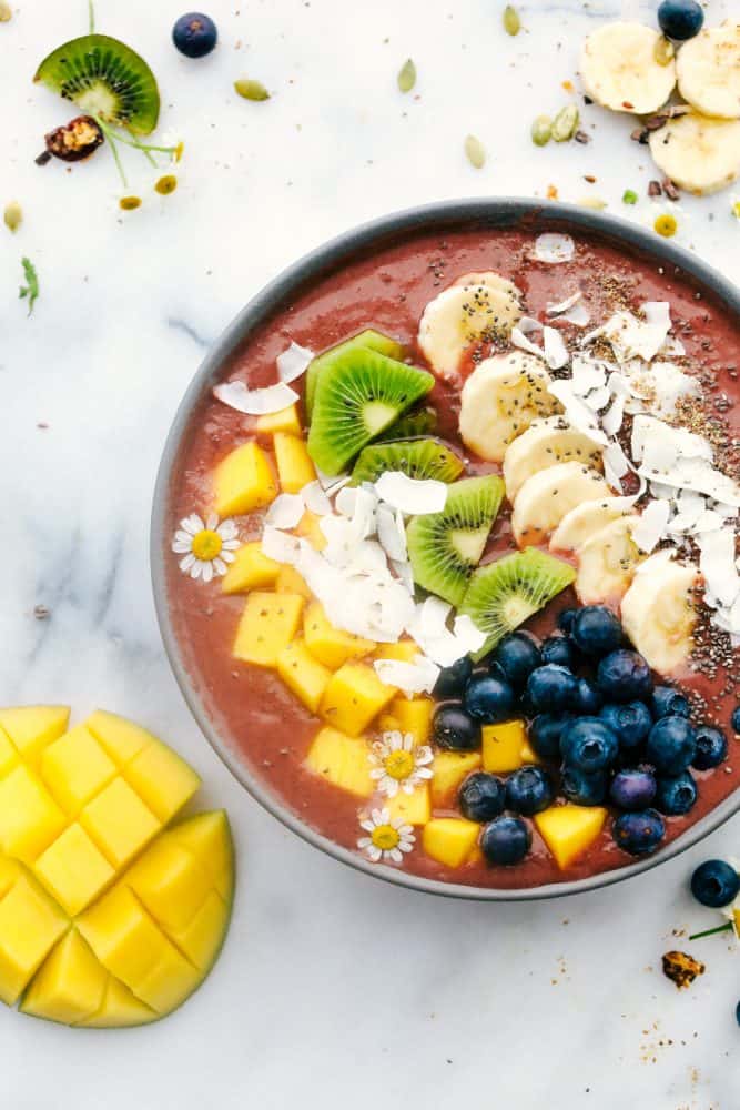 Tropical Mango acai bowl with fruit toppings and a fruit ingredients on the side.