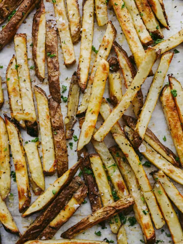 Baked fries topped with herbs laid out on parchment paper.