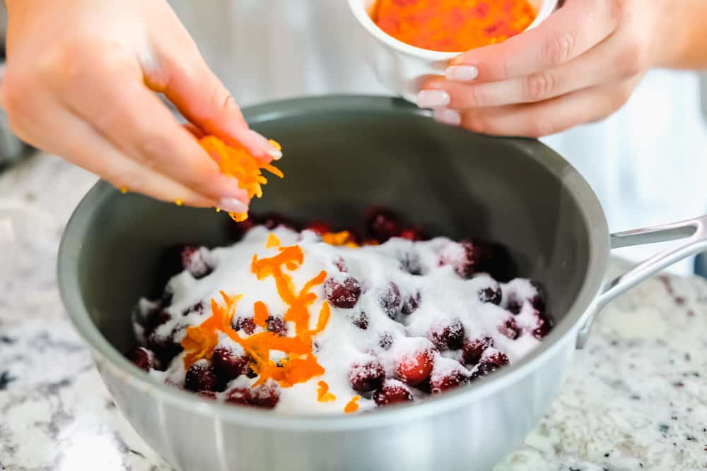 Cranberries in a pan with sugar and adding orange zest overtop.