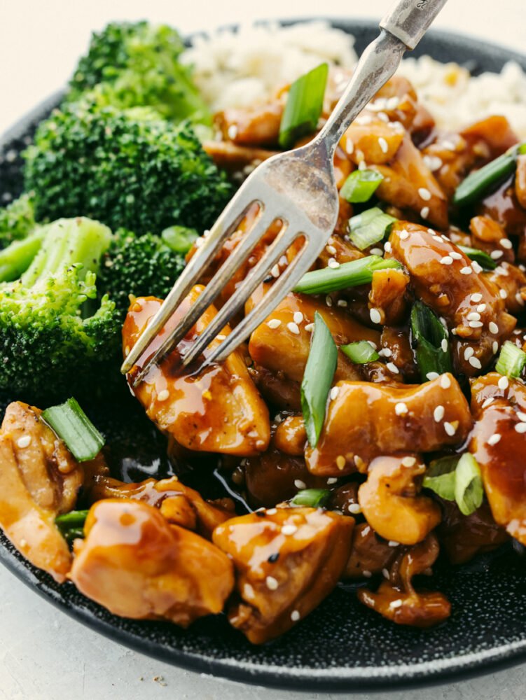 A close up of a teriyaki chicken bowl with a fork in a piece of chicken. 