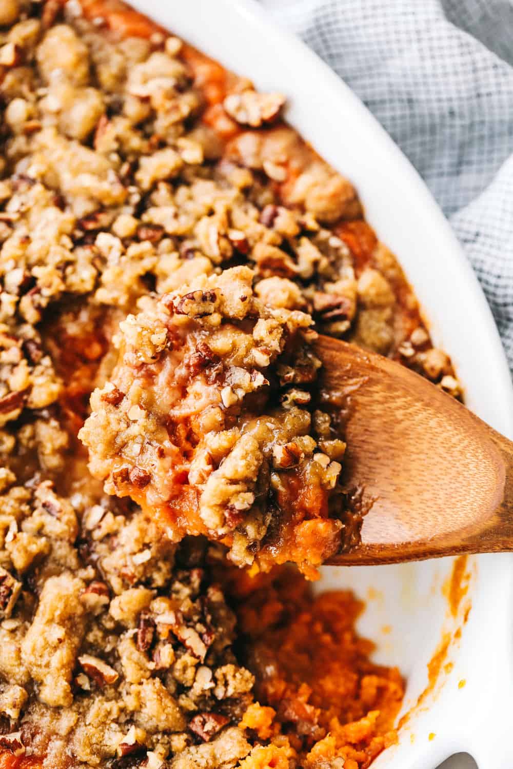 Taking a scoop of sweet potato casserole with a wooden spoon.