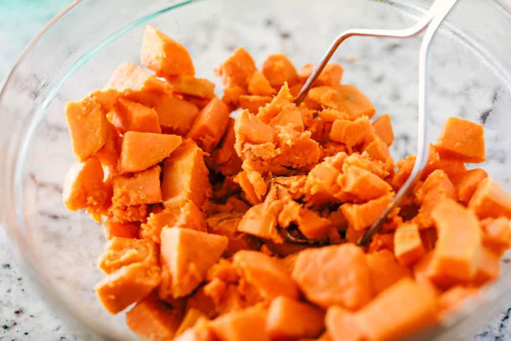 Mashing sweet potatoes in a clear bowl.