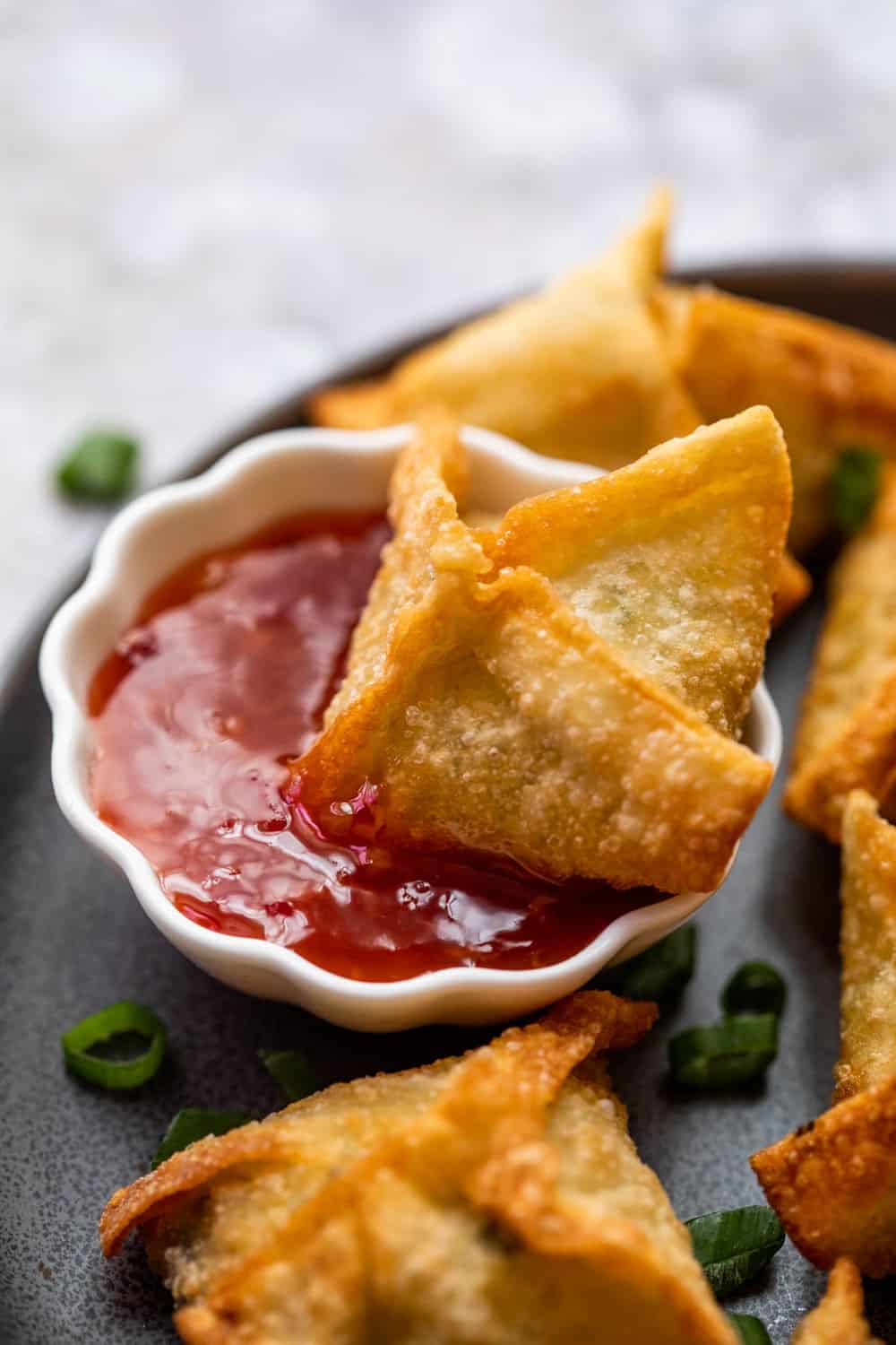 Crab rangoon being dipped in sweet and spicy sauce