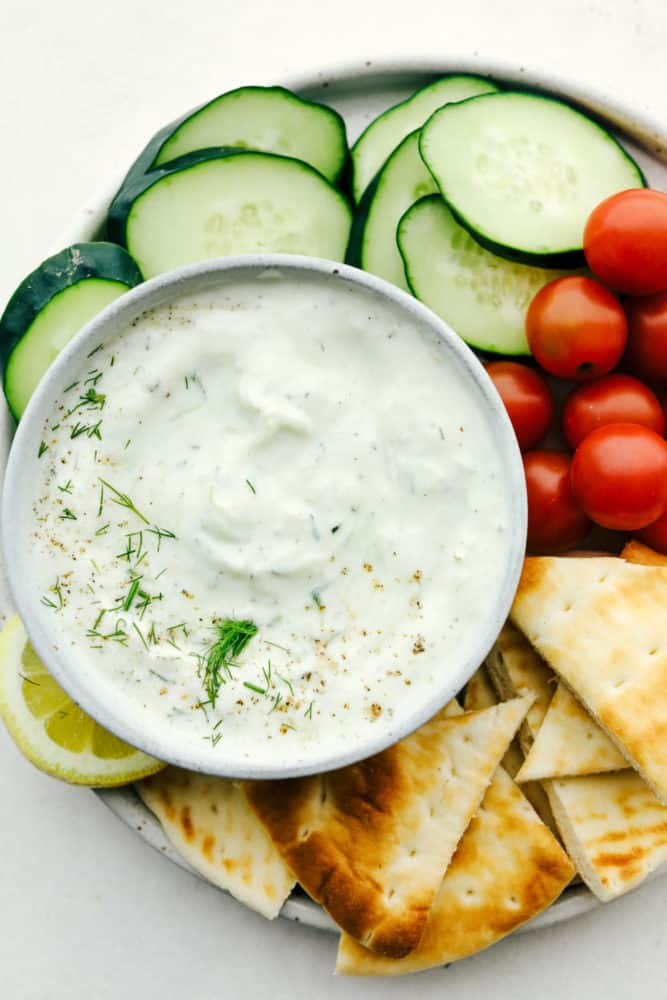 Close up on tzatziki sauce in a bowl on a veggie platter with pita.