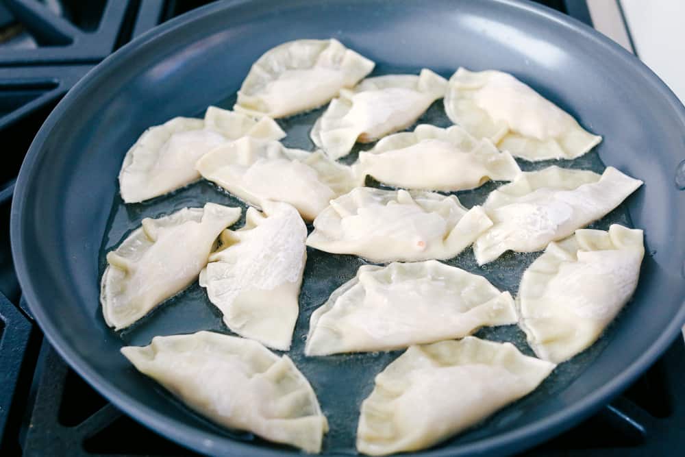 Potstickers being fried in a skillet.