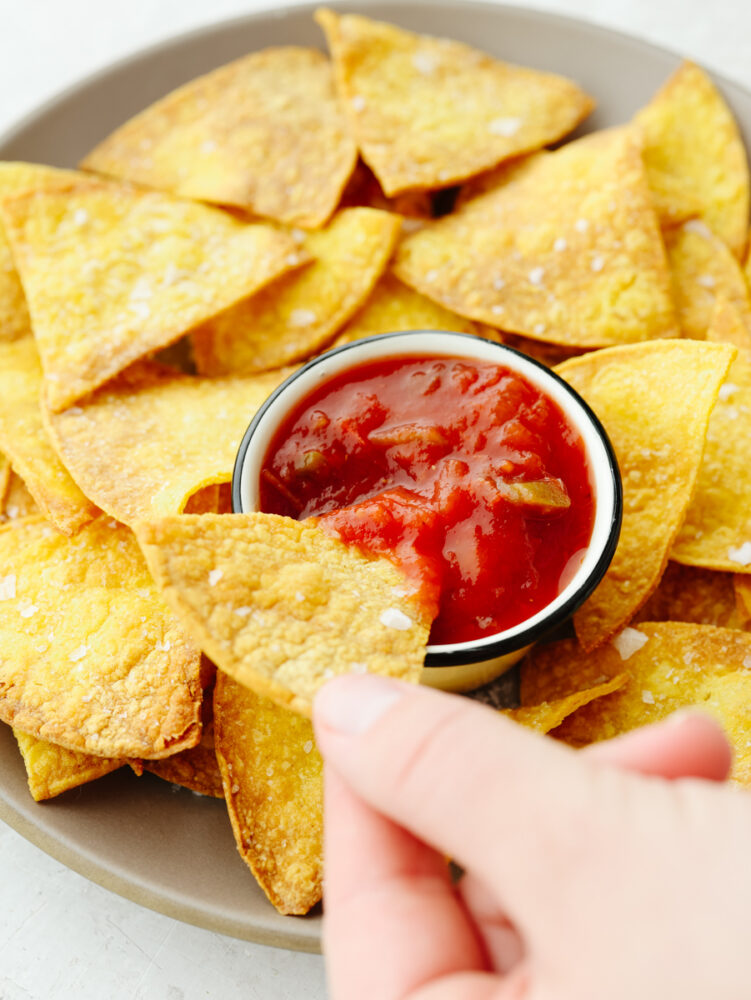 Air fryer tortilla chips on a light brown plate served with salsa.