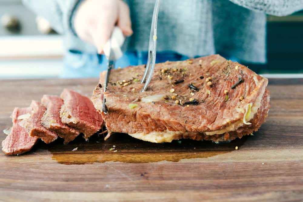 Corned beef being sliced on a wood cutting board. 