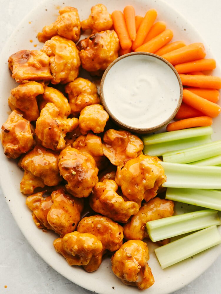 A platter with cauliflower wings, celery, carrots and some ranch dressing. 