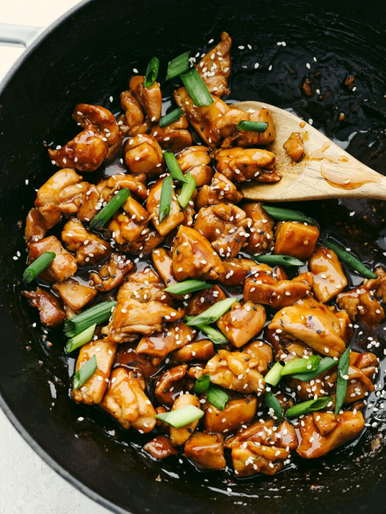 A pan of teriyaki chicken being stirred with a wooden spoon. 