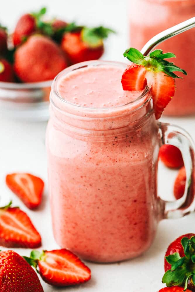 Strawberry smoothie in a glass mason jar with a metal straw. 