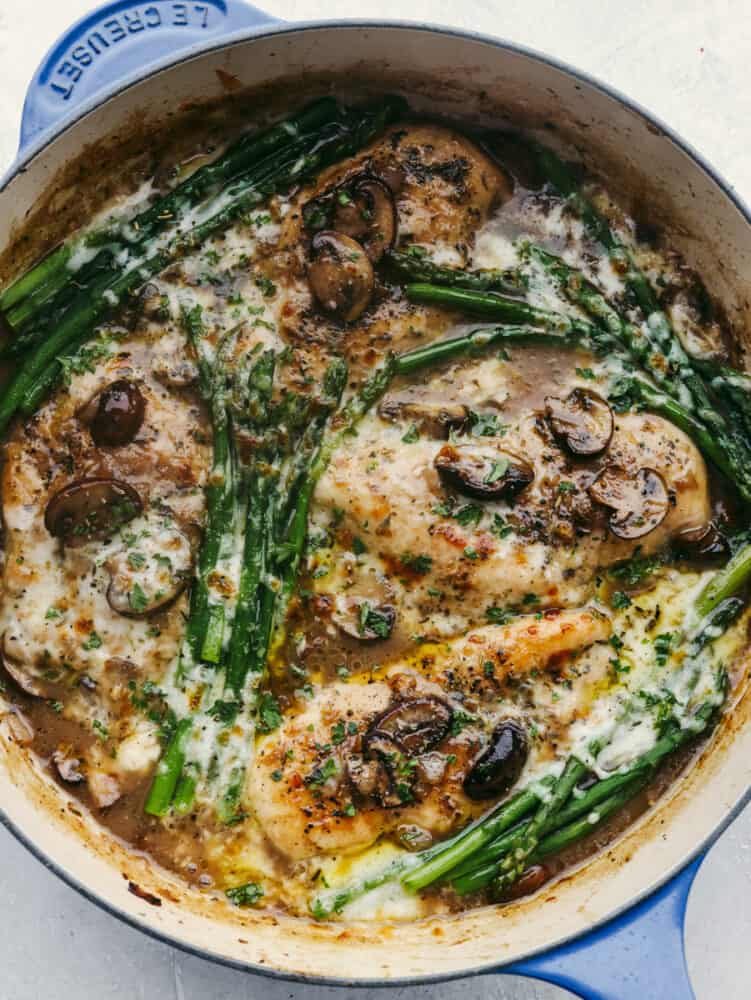 Chicken with mushrooms, cheese, and asparagus in a skillet.