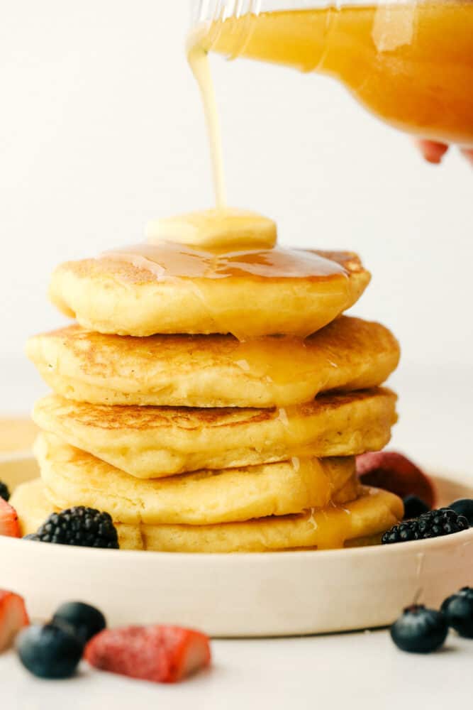 A stack of cornmeal pancakes with honey butter syrup being poured over the top. 