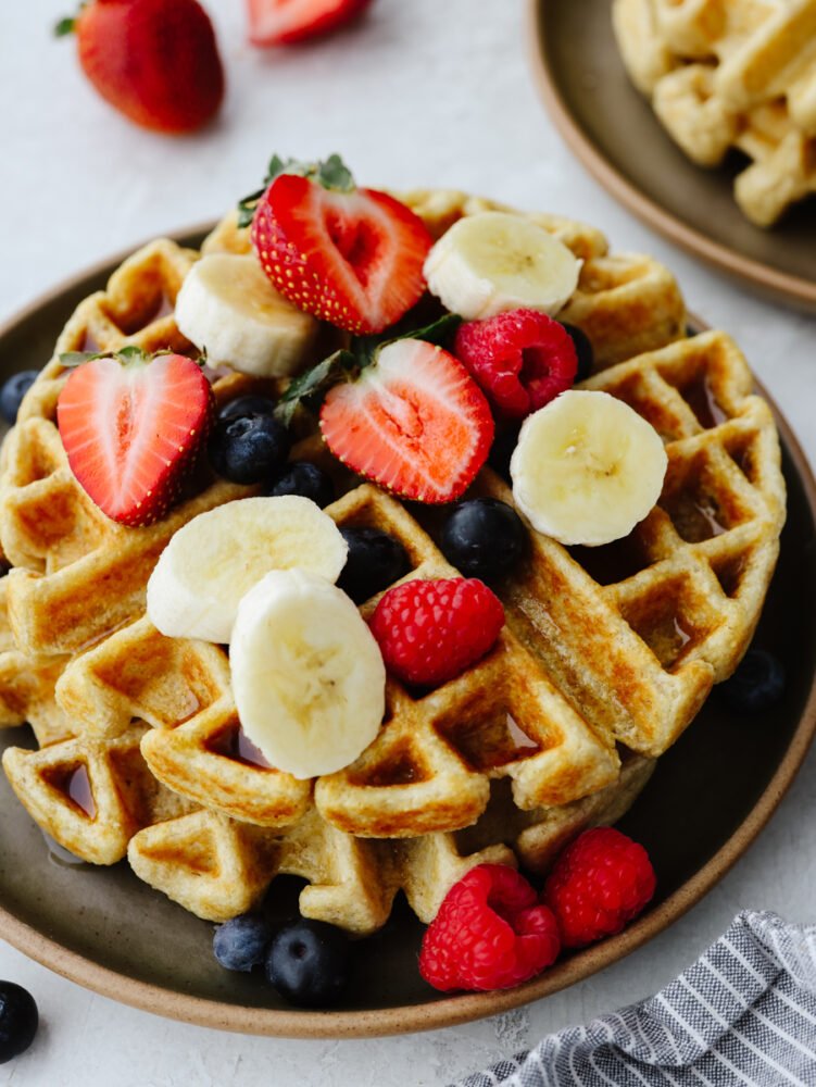 Waffles on a plate topped with bananas, blueberries, strawberries or raspberries. 