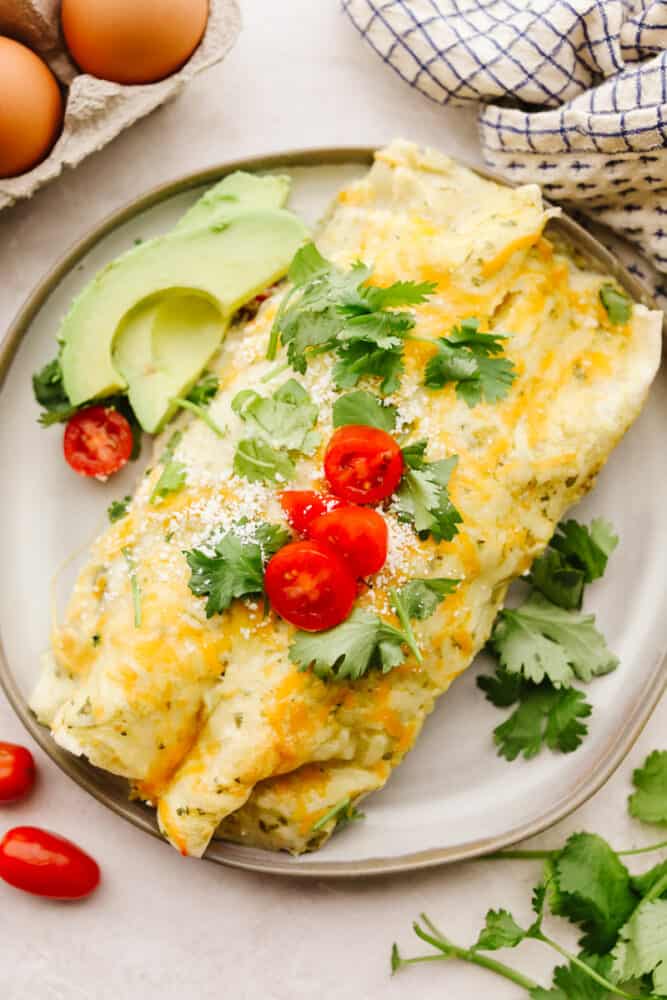 A plate with breakfast enchiladas garnished with cilantro, avocado and tomatoes. 