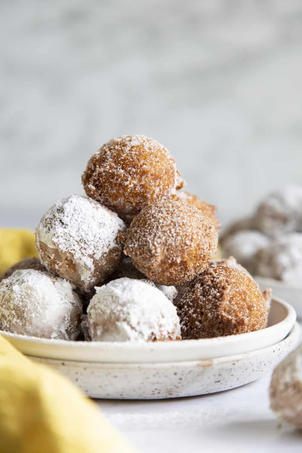 A plate full of powdered sugared and cinnamon sugared donut holes. 