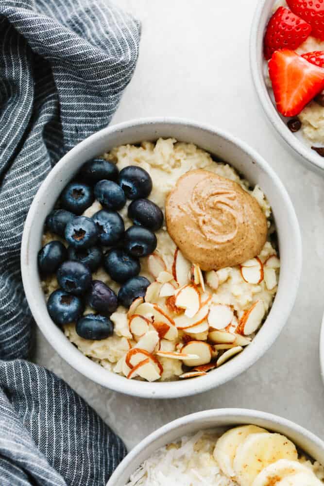 A bowl of oatmeal topped with almond slices, peanut butter, and blueberries.