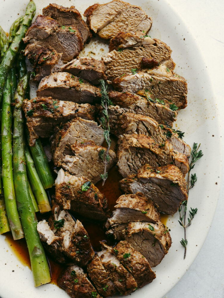 Sliced tenderloin on a white plate served with asparagus.