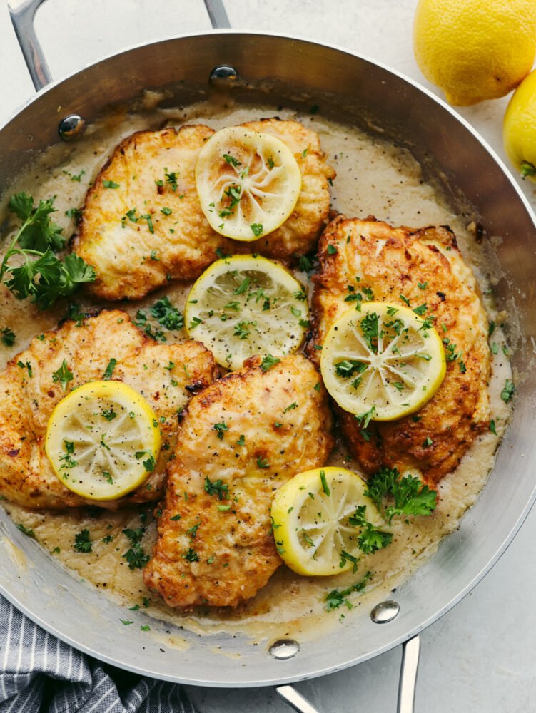 A pan with chicken Francese in a lemon sauce topped with lemon slices. 
