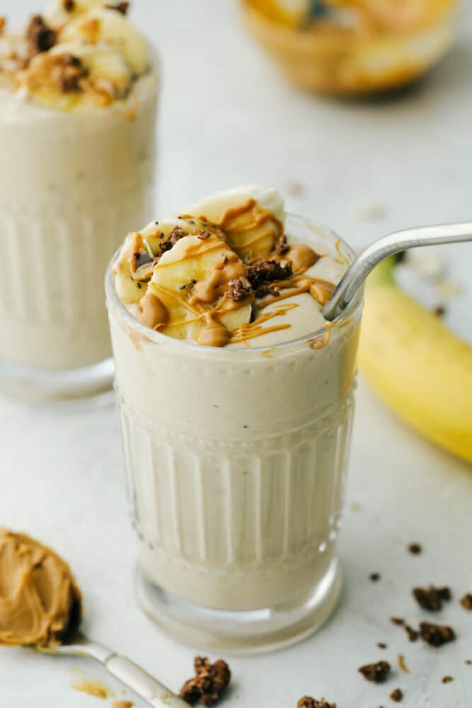 A Banana smoothie with a metal straw in a glass cup. 