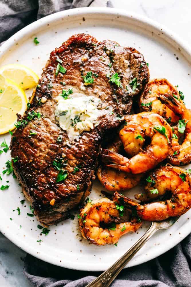 Steak and shrimp on a white plate with lemon slices on the side.