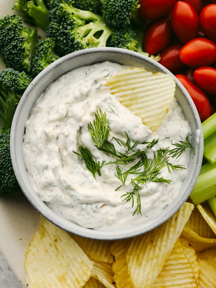 A top view of some dill dip on a platter with chips, broccoli, celery and cherry tomatoes. 