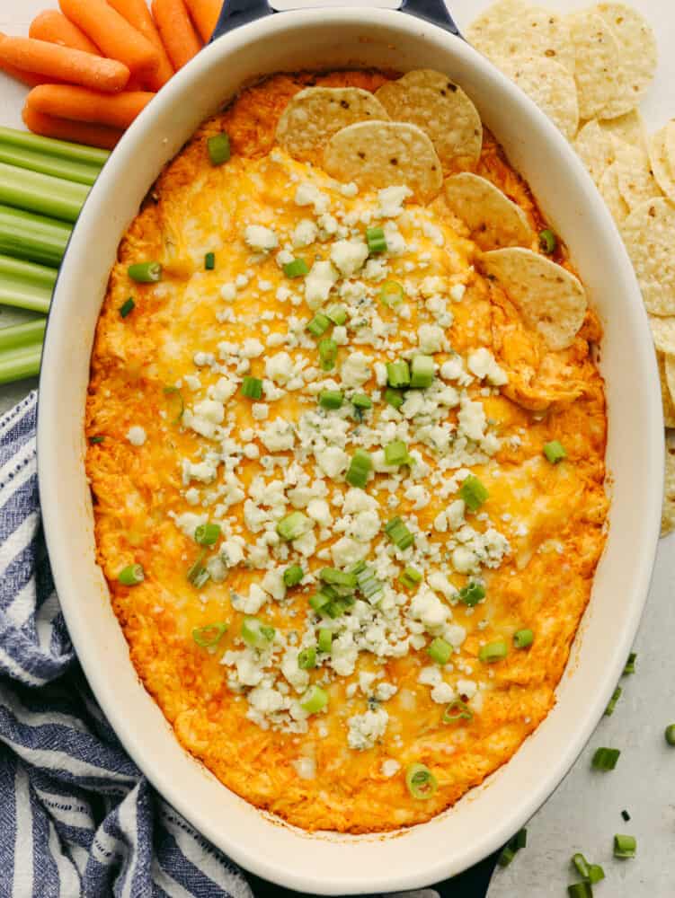 A dish of buffalo chicken dip with green onions and blue cheese crumbles. 