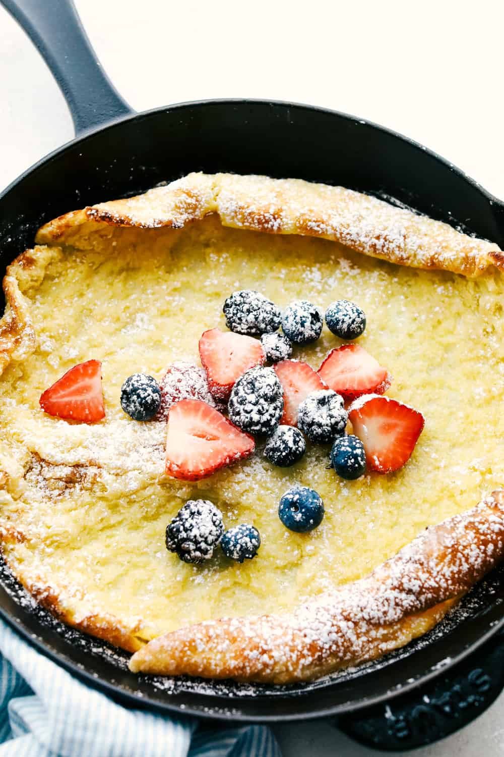 German pancake in a frying pan with a variety of berries overtop. 