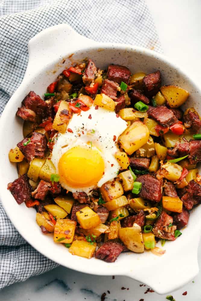 Corned beef hash with an egg on top in a white skillet.